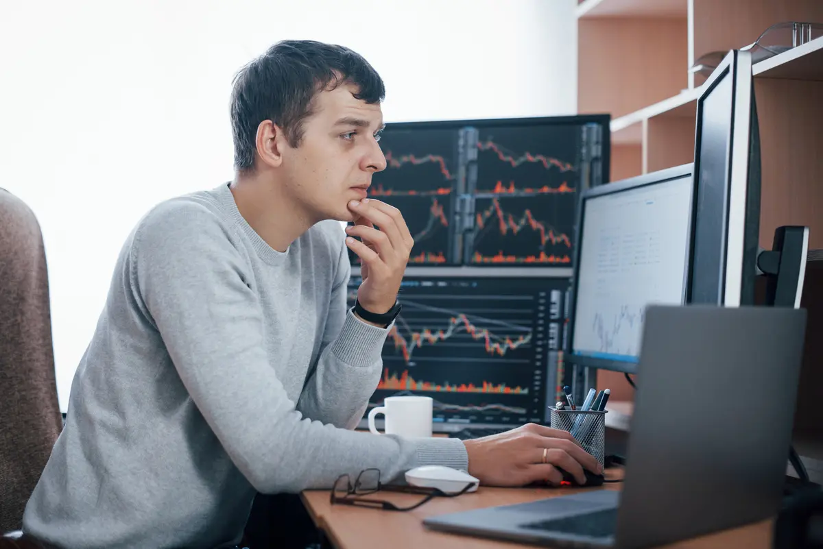 Trader studying charts across several monitors